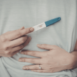 Paar umarmt sich und Frau hat Schwangerschaftstest in der Hand