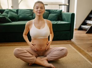 Frau sitzt auf Boden im Schneidersitz mit Händen auf Bauch