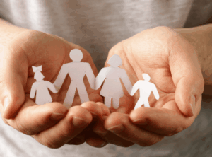 Hände zeigen Papiermännchen von einer vierköpfigen Familie